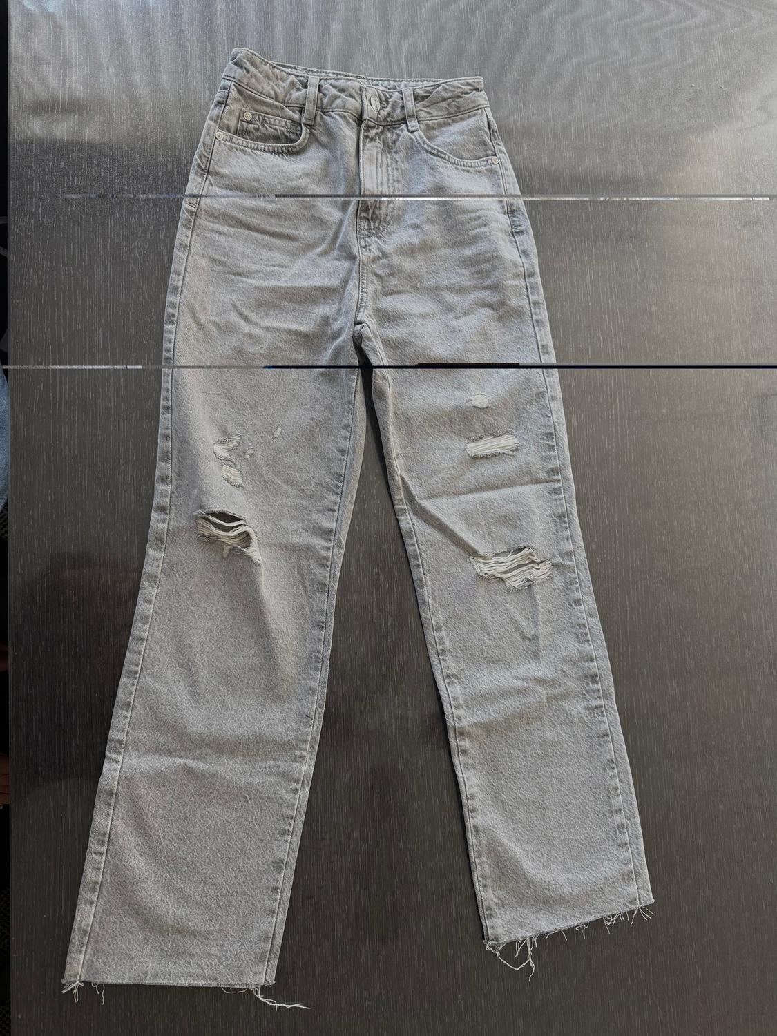 Distressed gray jeans with rips on the legs, placed on a dark surface.