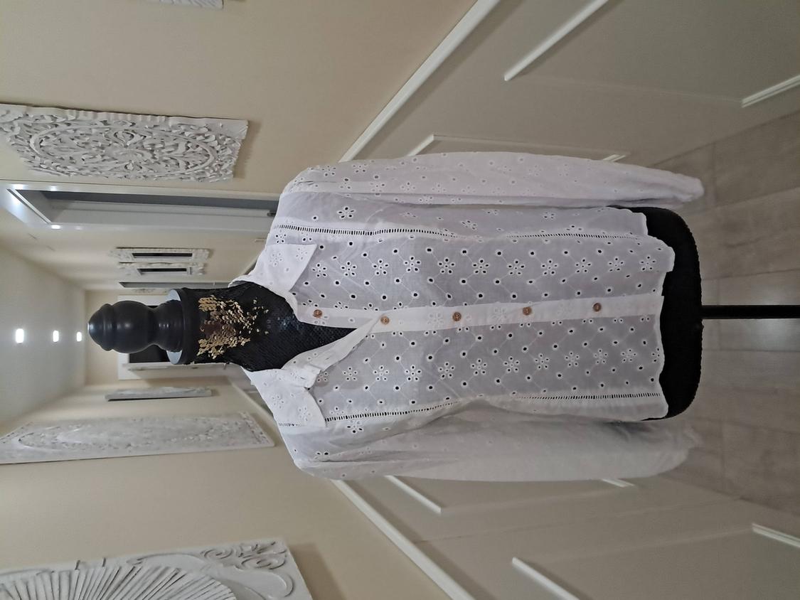 Mannequin in a white floral lace blouse with brown buttons in a hallway decorated with artistic wall panels.