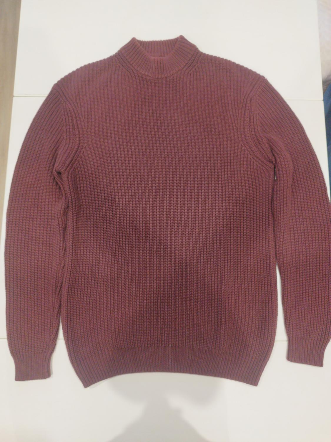 Chunky knit burgundy jumper on a white surface, with a high neck and long sleeves.