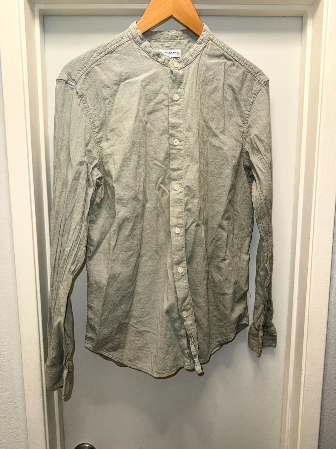 Light gray long-sleeve shirt with a mandarin collar and buttons, hanging on a wooden hanger in front of a white door.