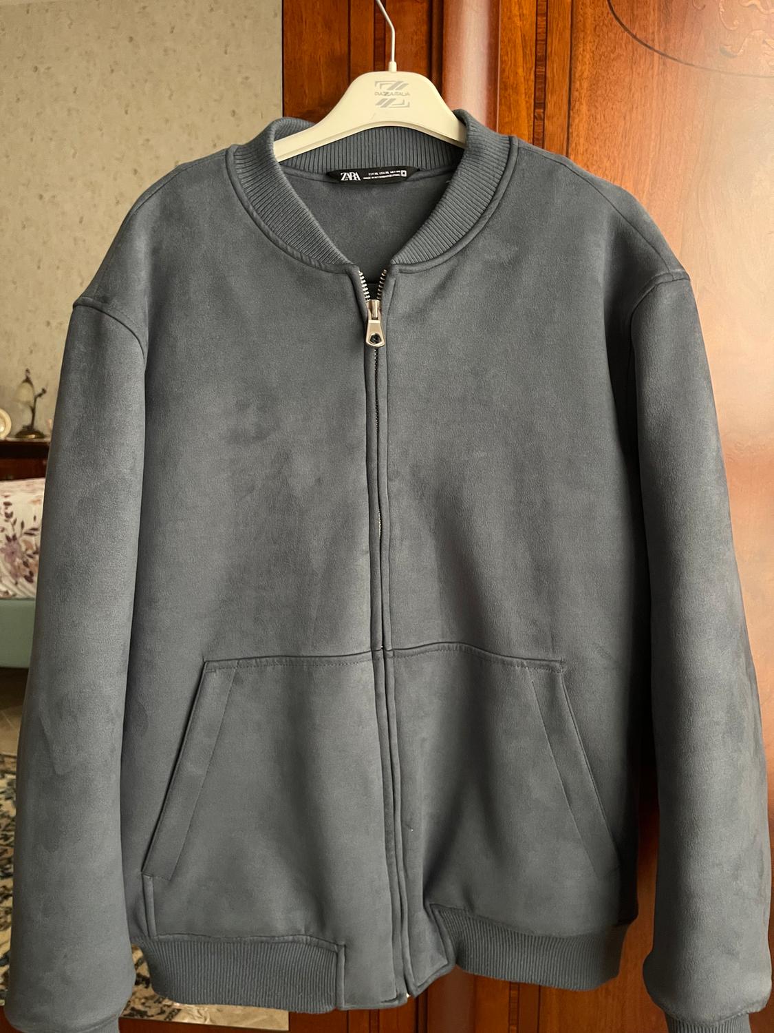 Grey jacket with zip and front pockets, hanging on a white hanger in a wooden wardrobe.