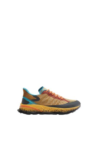 Trainers in shades of brown, blue, and orange with a black sole and speckled details. White background.