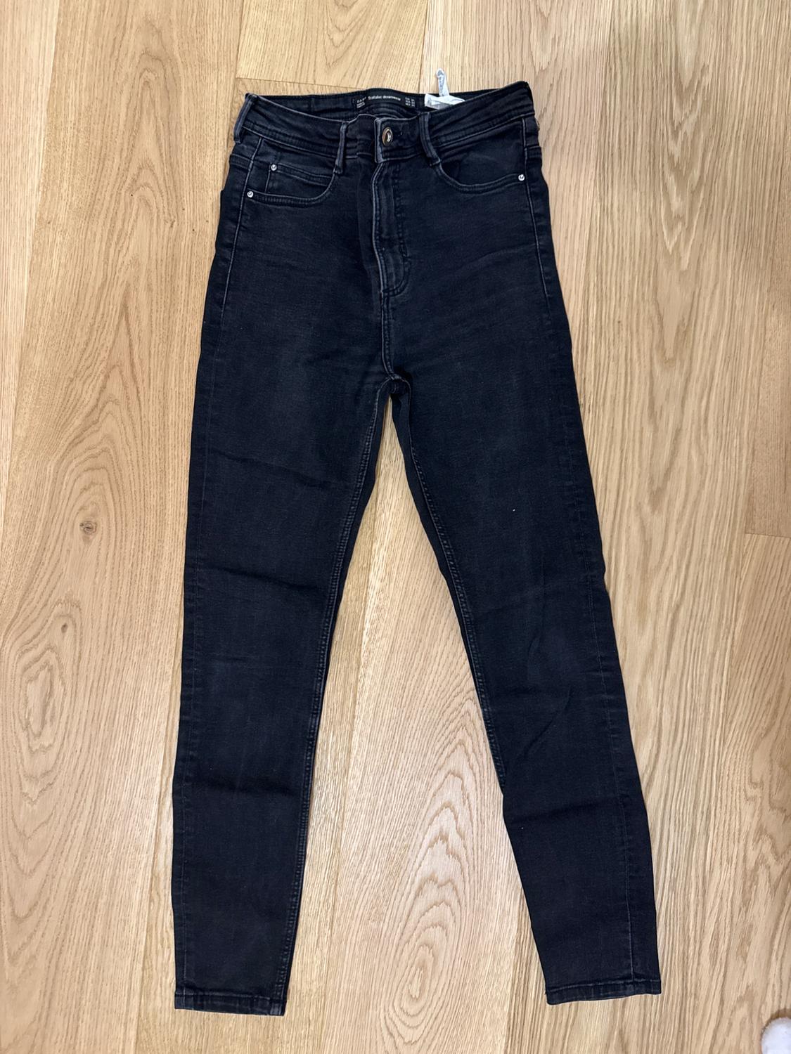 Black slim-fit jeans on a light wooden floor.