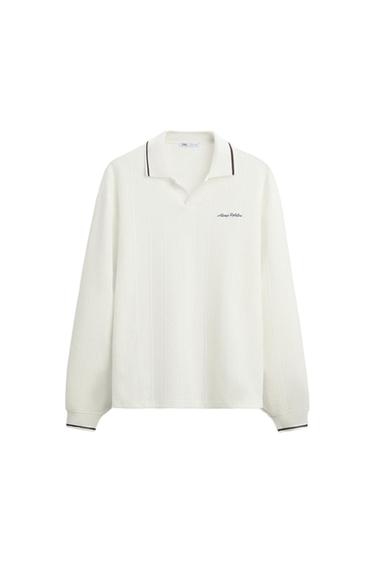White long-sleeved polo neck jumper with dark trim. "Always Positive" text embroidered on the chest. White background.