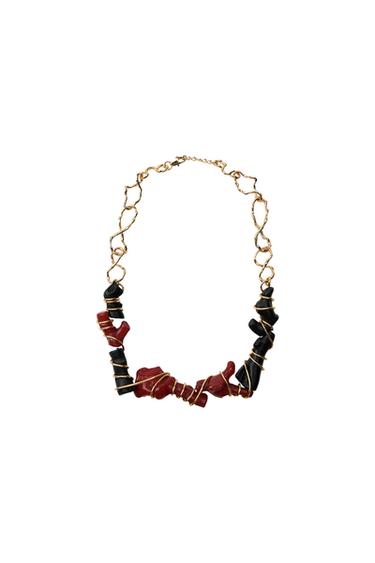Gold chain necklace with irregular links and black and red pieces wrapped in gold wire on a white background.