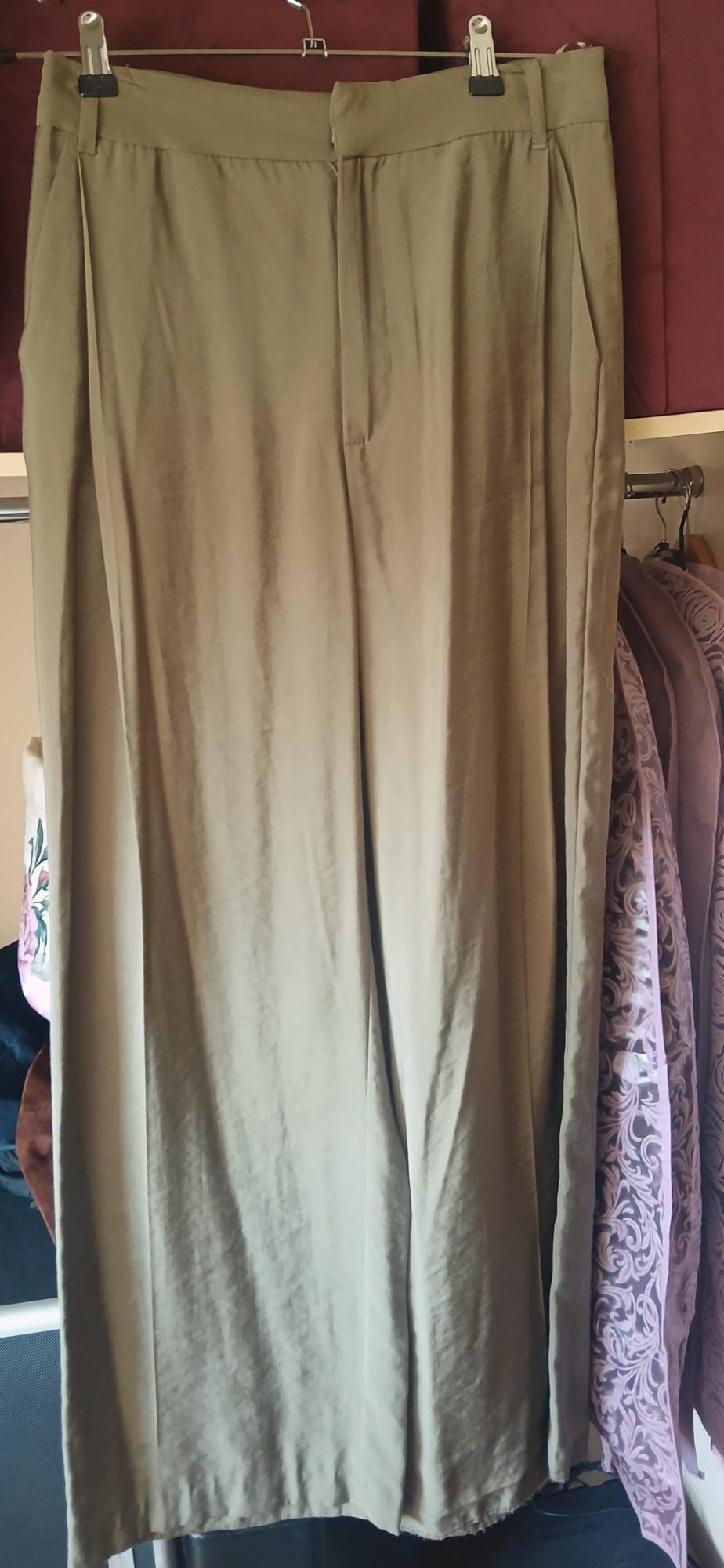 Long beige trousers hanging on a hanger, with a background of decorative purple curtains.