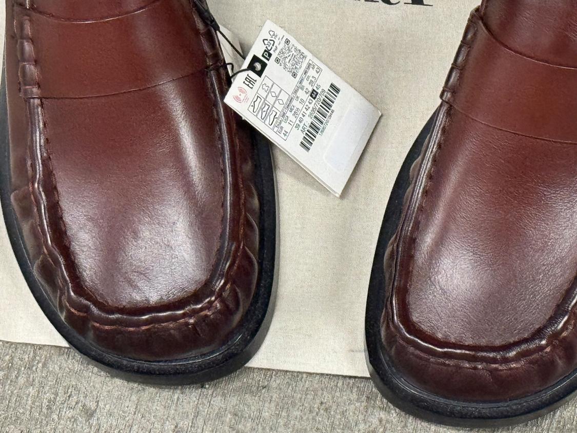 Close-up of brown leather loafer-style shoes with a product label showing the ART code: 2635/720/709, on a light surface.