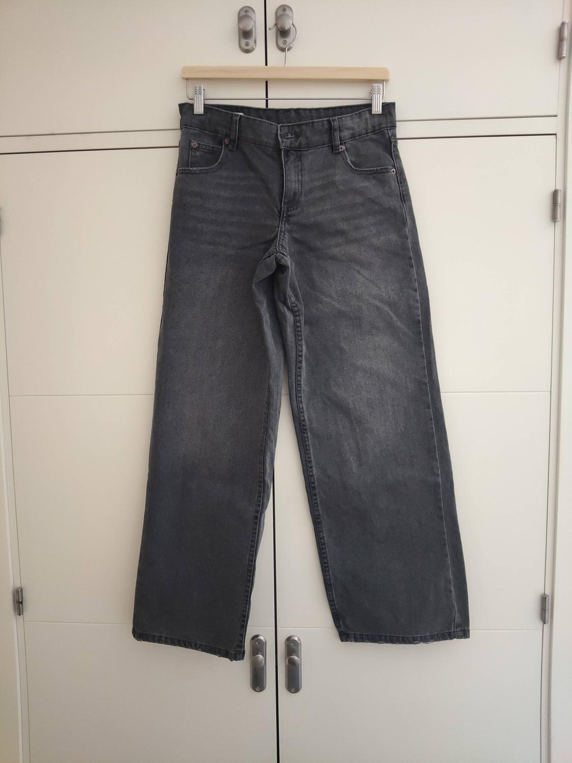 Grey wide-leg jeans hanging on a wooden hanger in front of a white wardrobe.