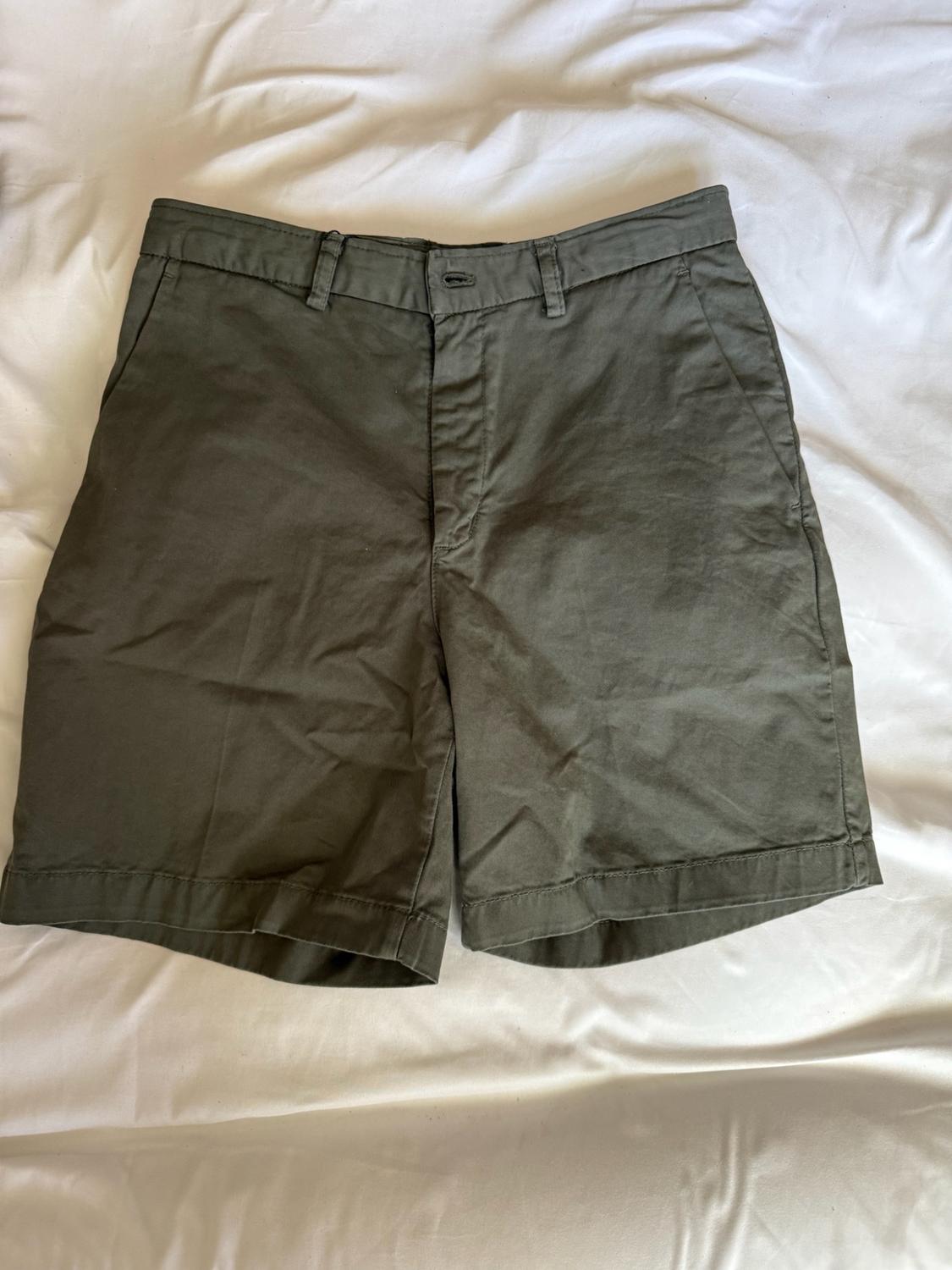 Dark green shorts on a crumpled white sheet. Casual style with a button fastening, belt loops and pockets.