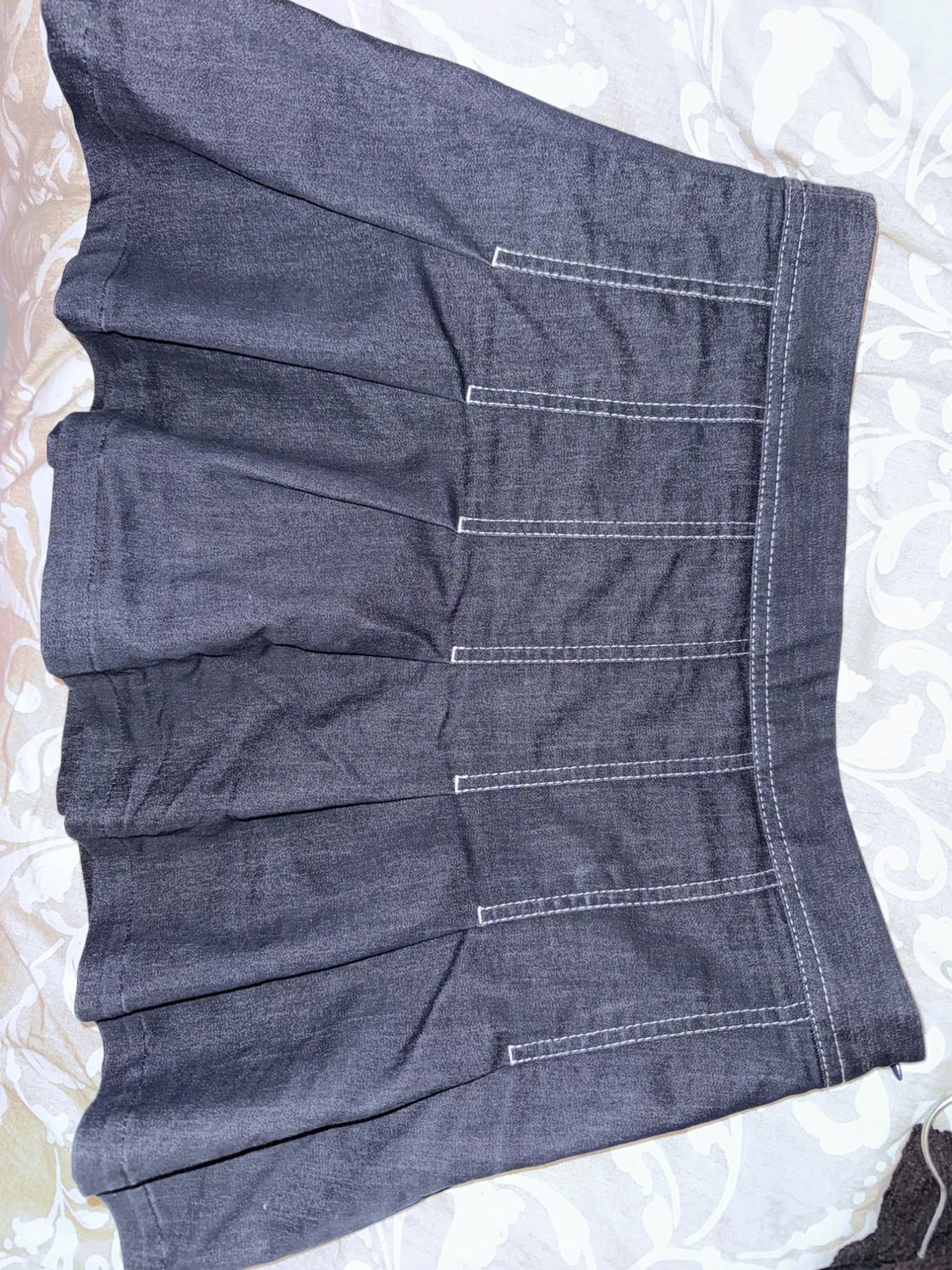 Grey denim skirt with pleats and visible stitching, on a surface with a floral design in light tones.