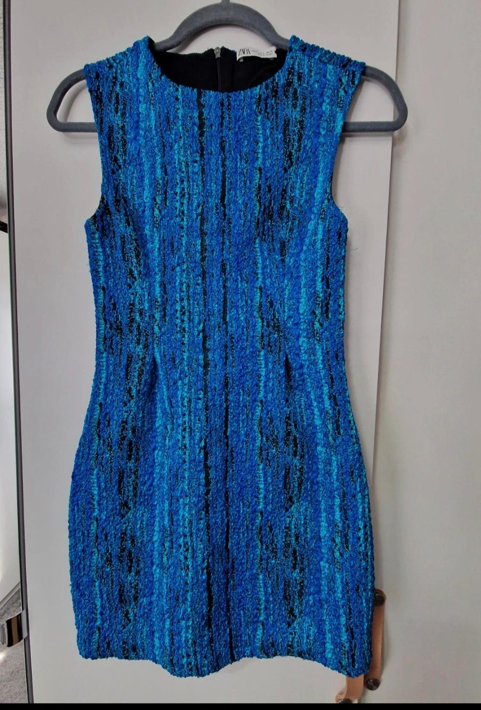 Blue sleeveless textured dress, hanging on a black hanger against a white background.