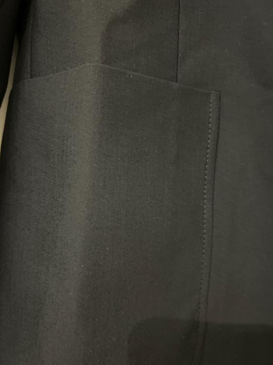 Close-up of a pocket on a dark fabric garment, showing stitching details and material texture.