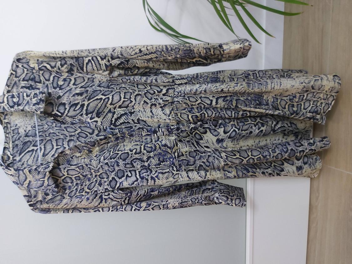 Μονοσόρτς μακρυμάνικο με snake print σε αποχρώσεις του μπεζ και του μπλε, κρεμασμένο σε κρεμάστρα. Λευκό φόντο με πράσινο φυτό.