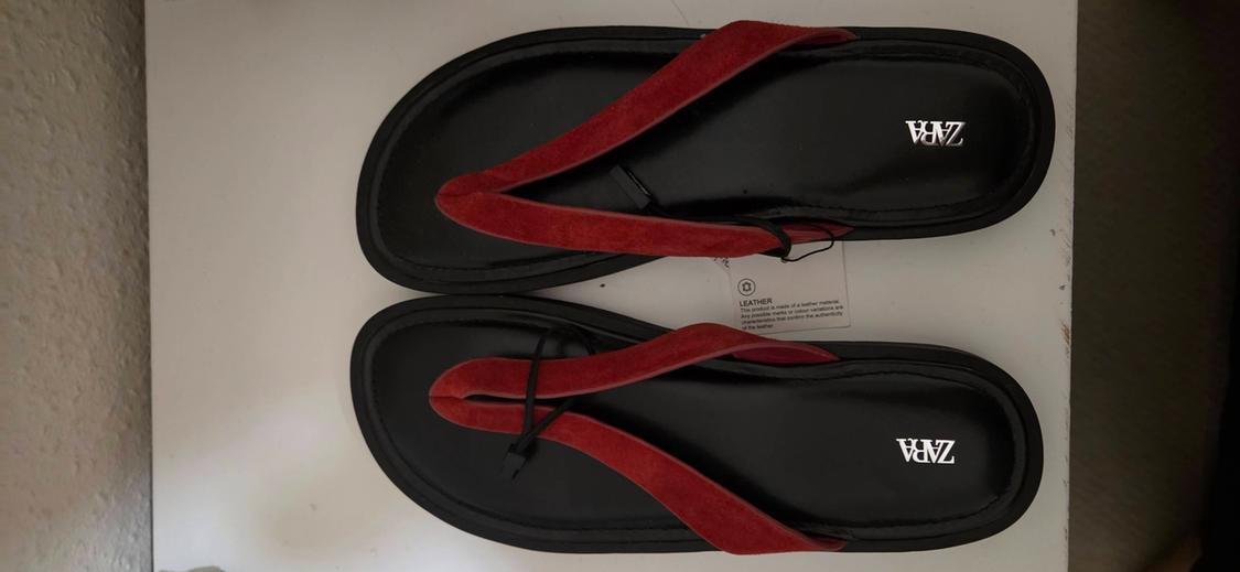 Sandals with a black sole and red straps on a white surface. Visible text: ZARA, LEATHER.