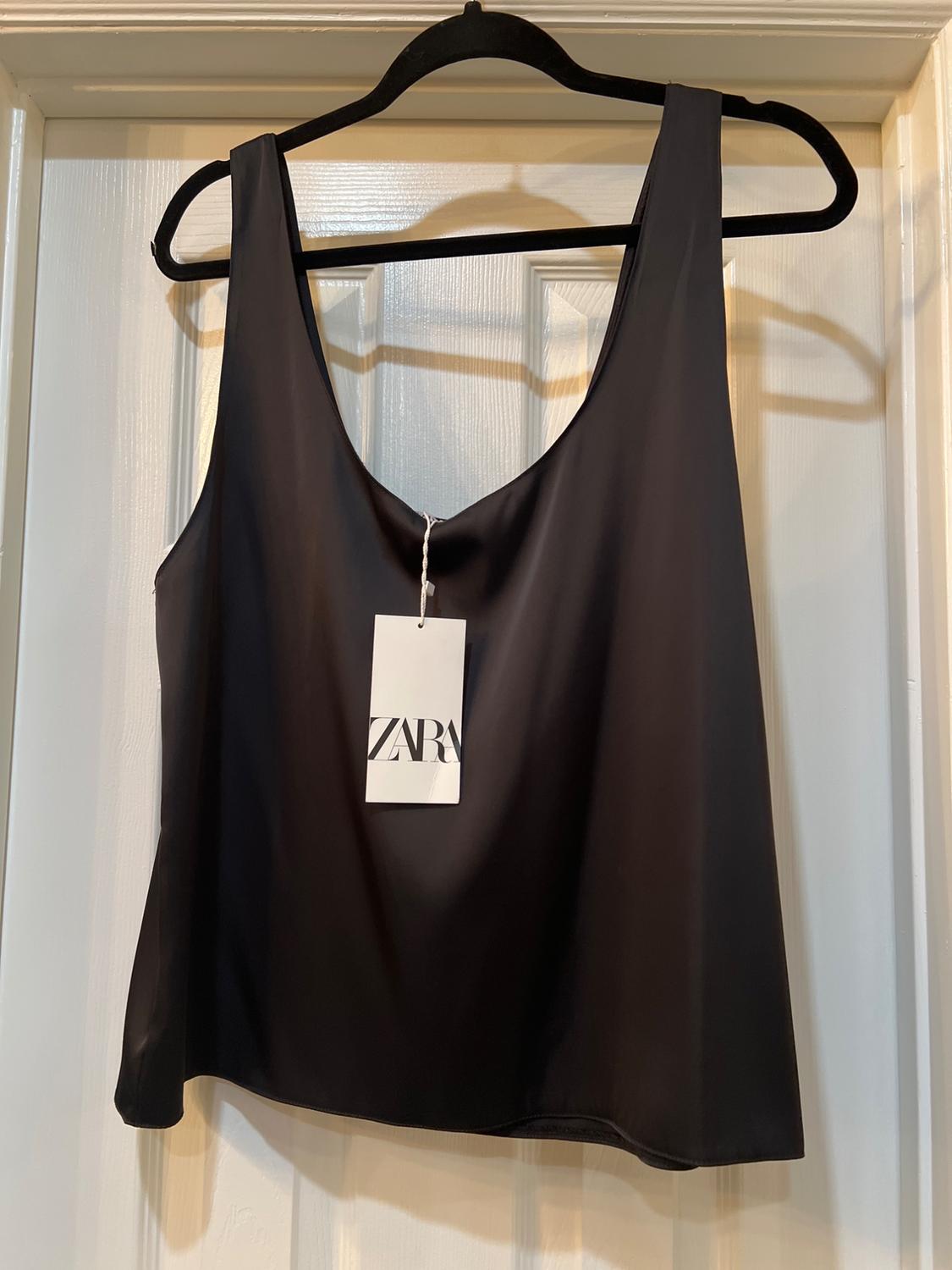 Black sleeveless top hanging on a black hanger, with a "ZARA" label, on a white door.