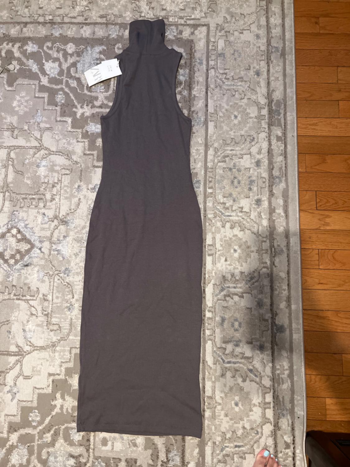 Sleeveless, dark gray maxi dress with a high neckline, placed on a decorative gray and beige rug. Foot visible in the lower right corner.