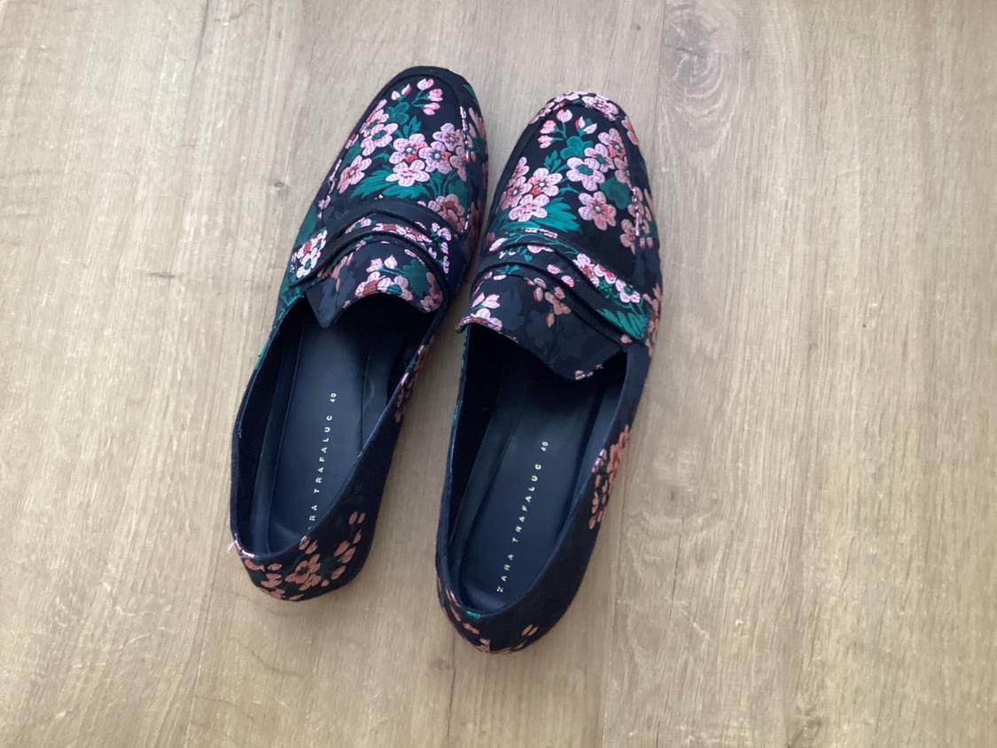 Black shoes with a pink and green floral pattern on a wooden floor. Visible text: "ZARA TRAFALUC".