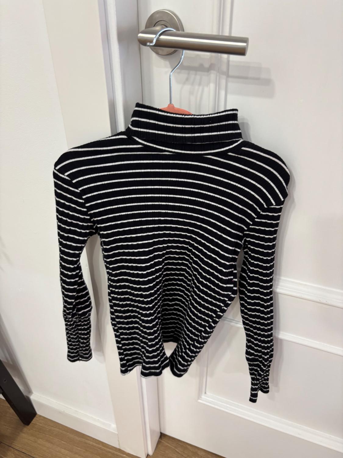 Black and white striped jumper hanging on a hanger on the handle of a white door. White wall background and wooden floor.