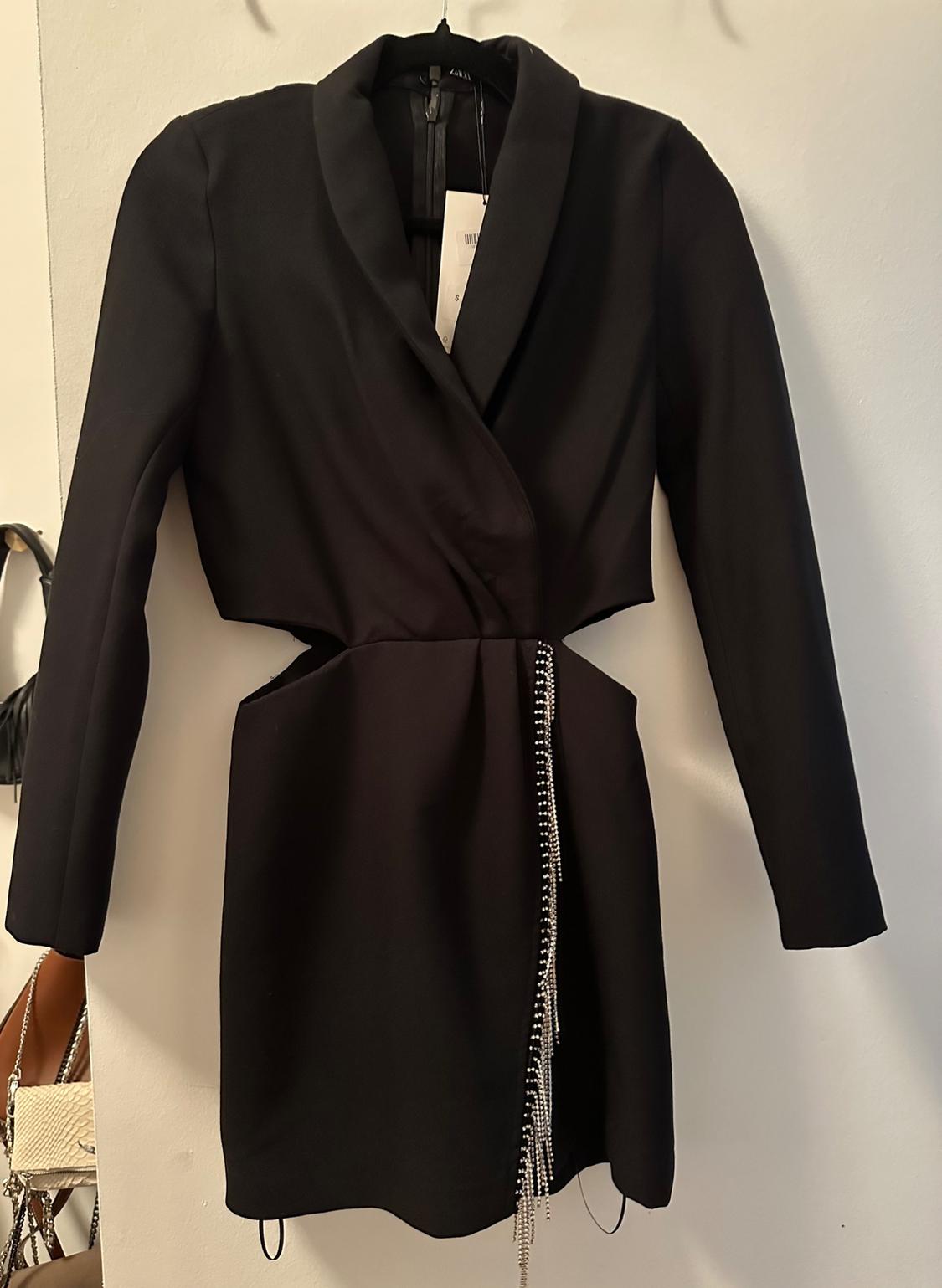 Front view of a black dress with lapel and shiny chain detail at the waist.