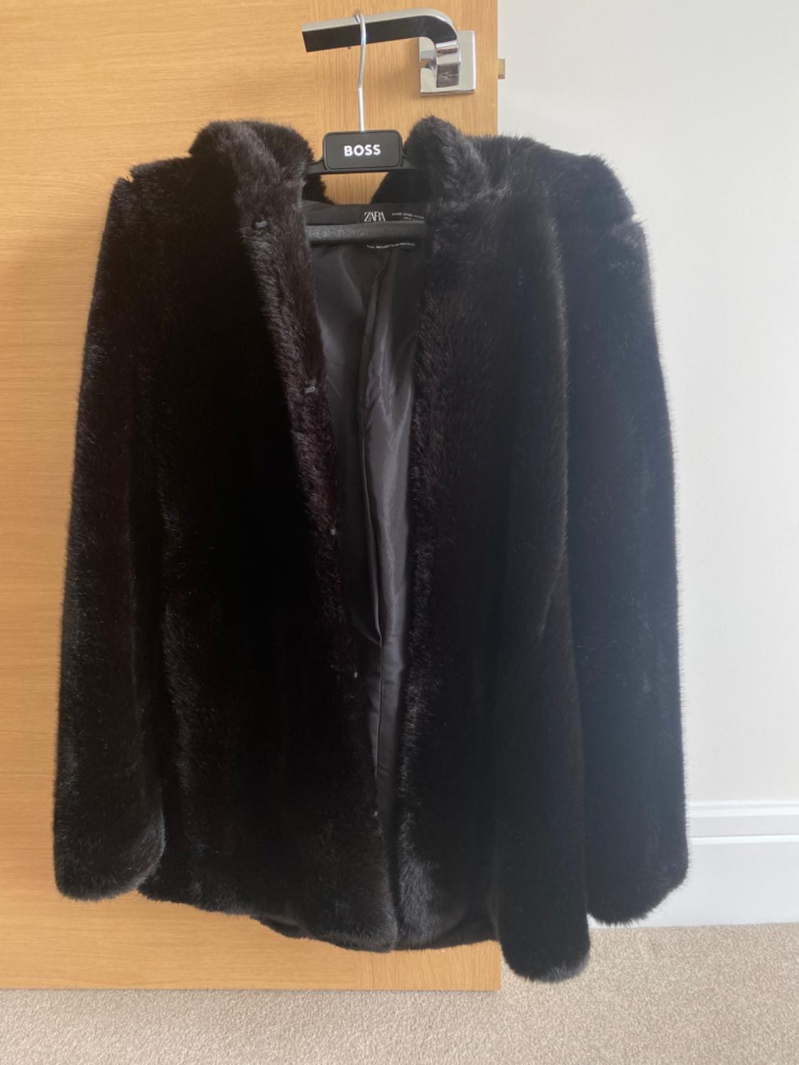 Front view of a black faux fur coat hanging on a hanger.