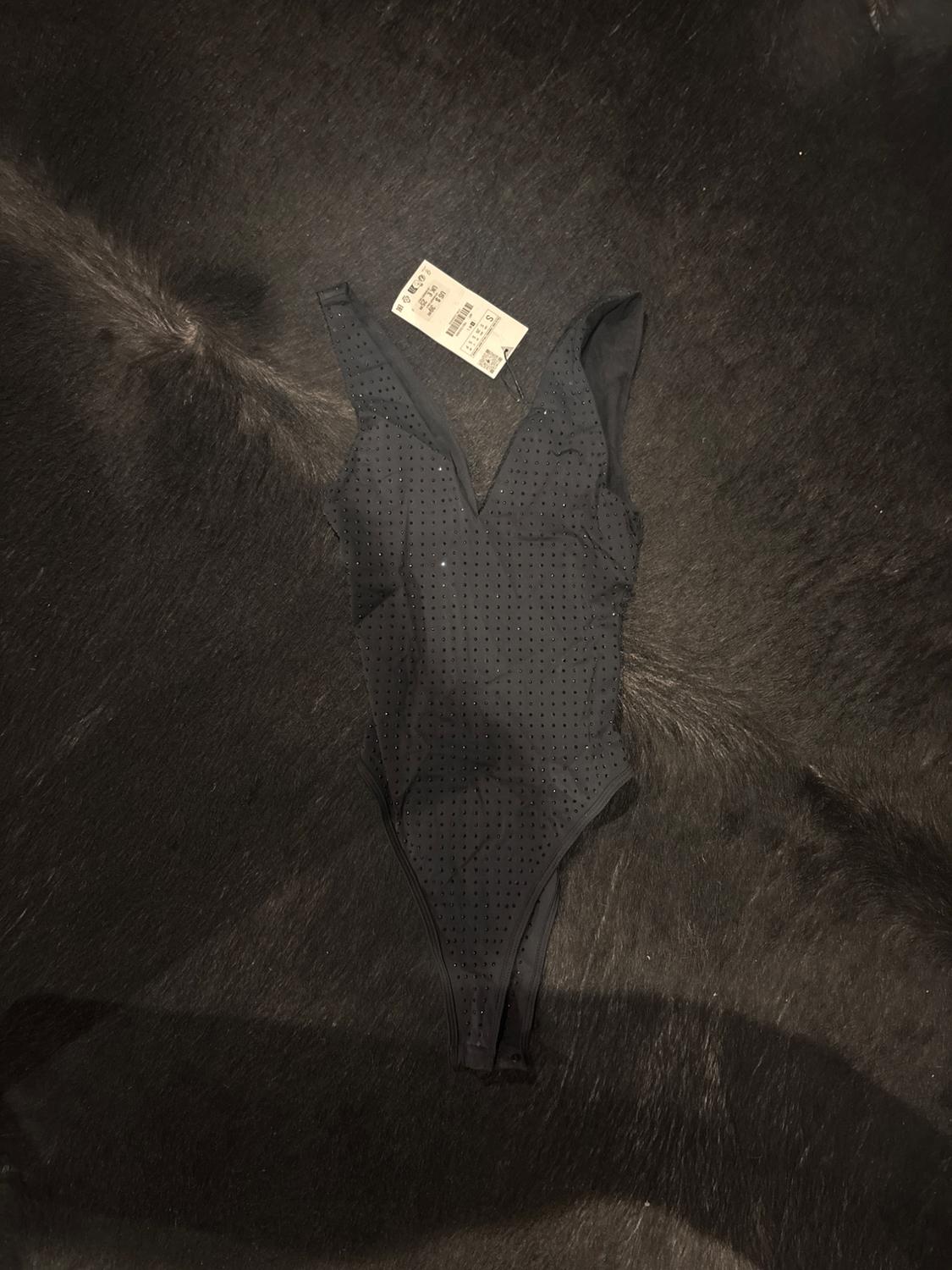 Black body with straps and polka dot design on a dark background. Visible label with text: "S €25.99".