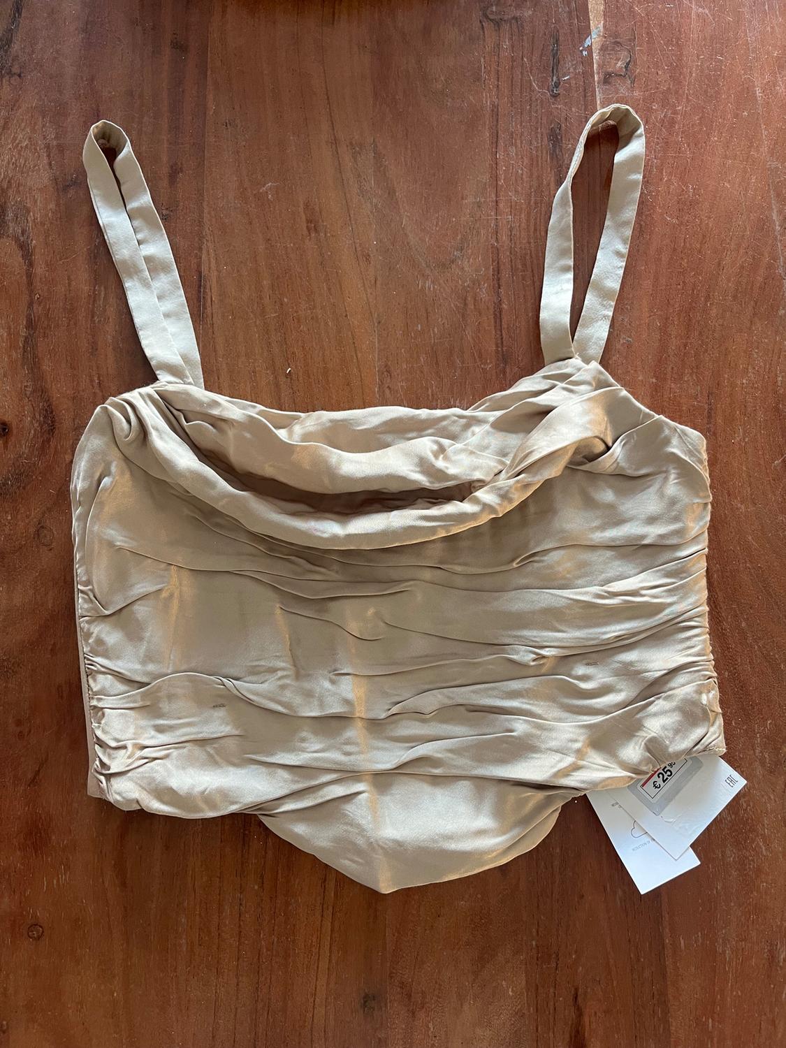 Beige camisole top with draping on a wooden table. Visible tag with price of £25.99.