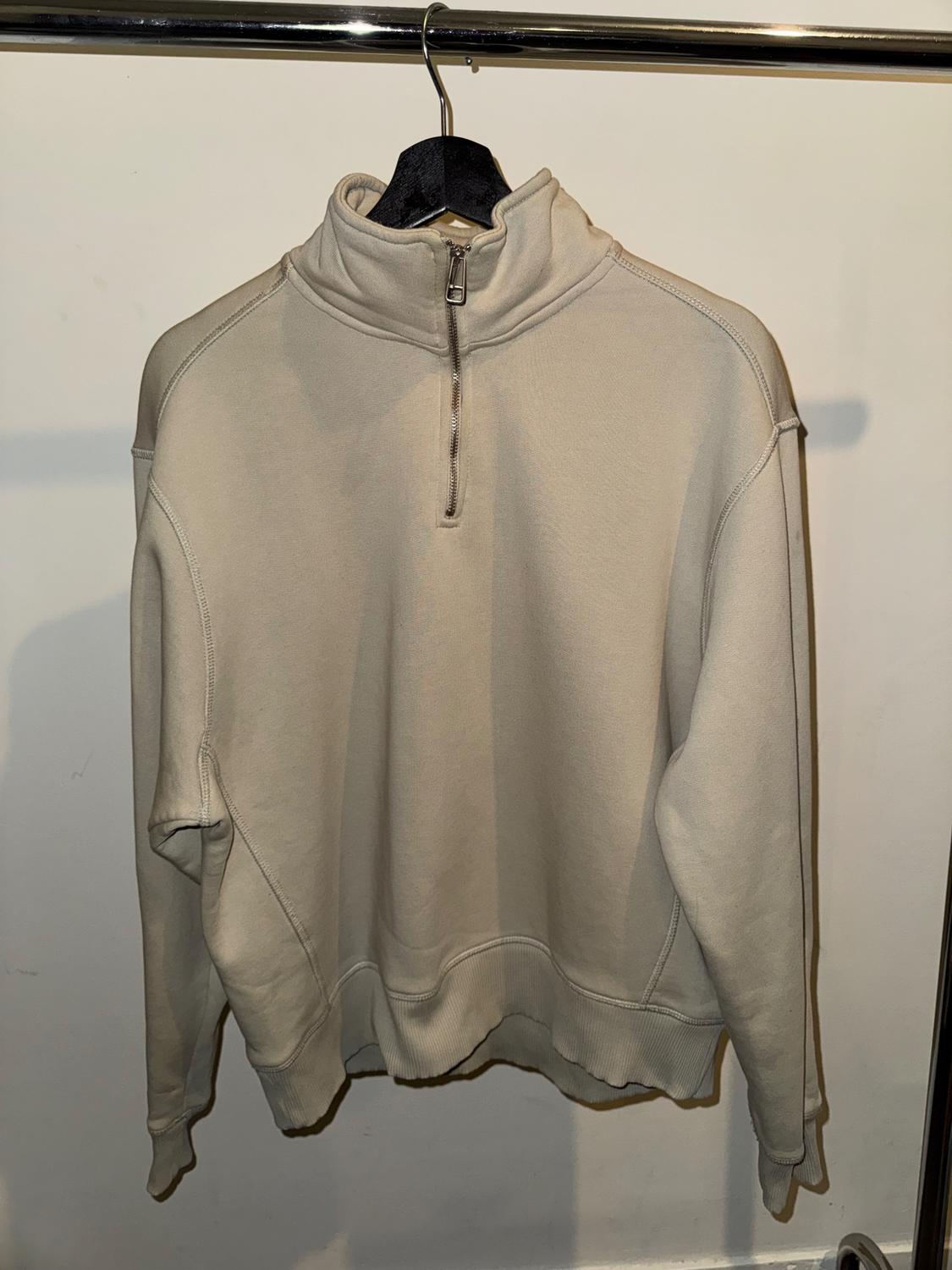Beige sweatshirt with a short zip and high neck, hanging on a black hanger against a white background.