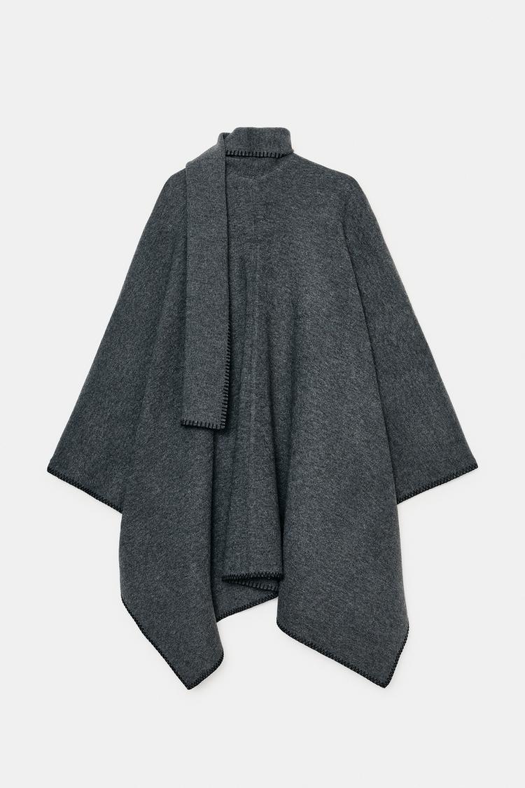 Přední pohled na šedou pelerínu s integrovanou šálou a kontrastním prošíváním. Asymetrický design.