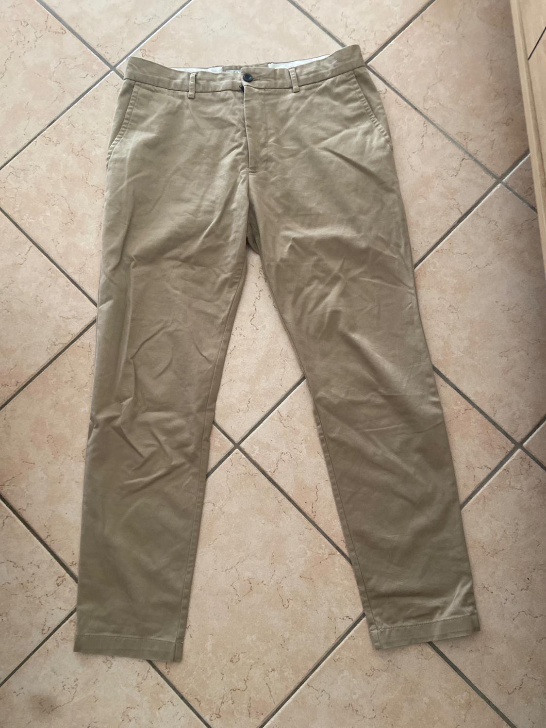 Beige chinos on a light tiled floor. Classic design with side pockets and button fastening.