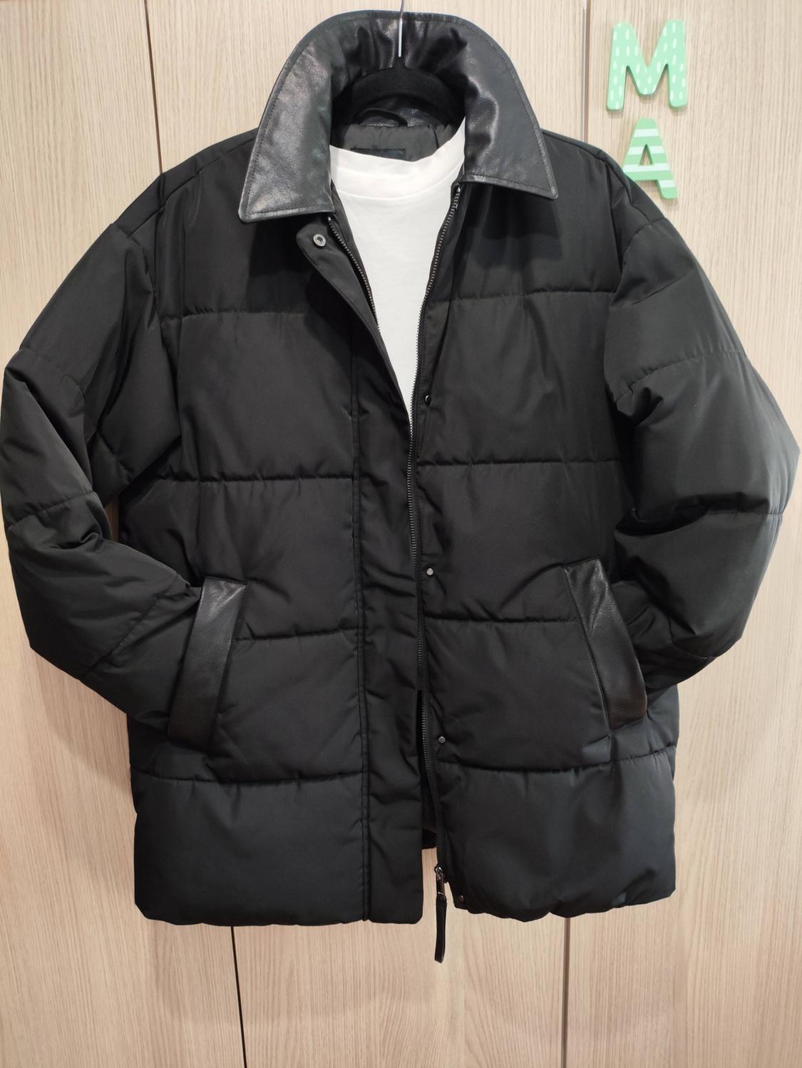 Μαύρο καπιτονέ μπουφάν με γιακά σε αντίθεση πάνω από λευκό μπλουζάκι, κρεμασμένο σε ξύλινη ντουλάπα με τα γράμματα M και A.