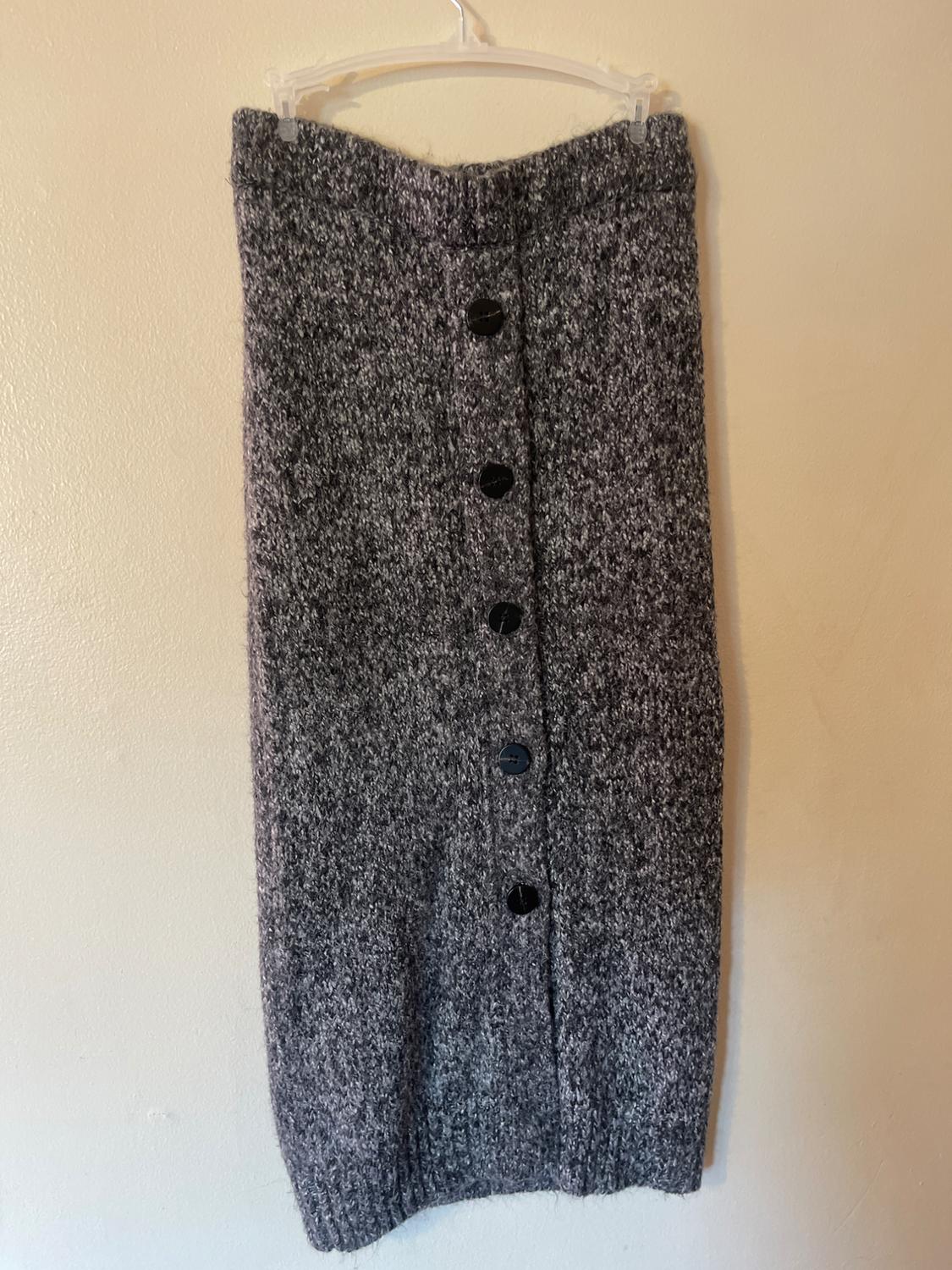 Gray knit skirt with black buttons down the front, hanging on a white hanger against a beige wall.