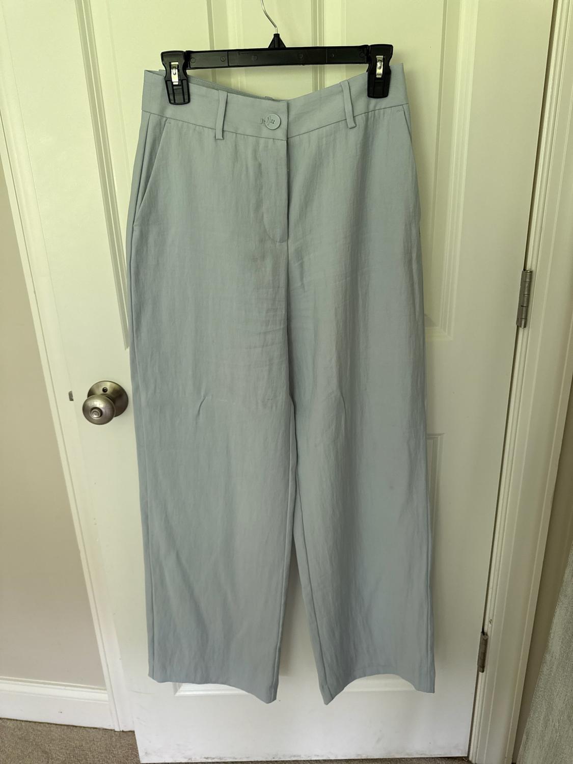 Light blue wide-leg pants hanging from a hanger on a white door. High-waisted design with belt loops, pockets, and a button closure.