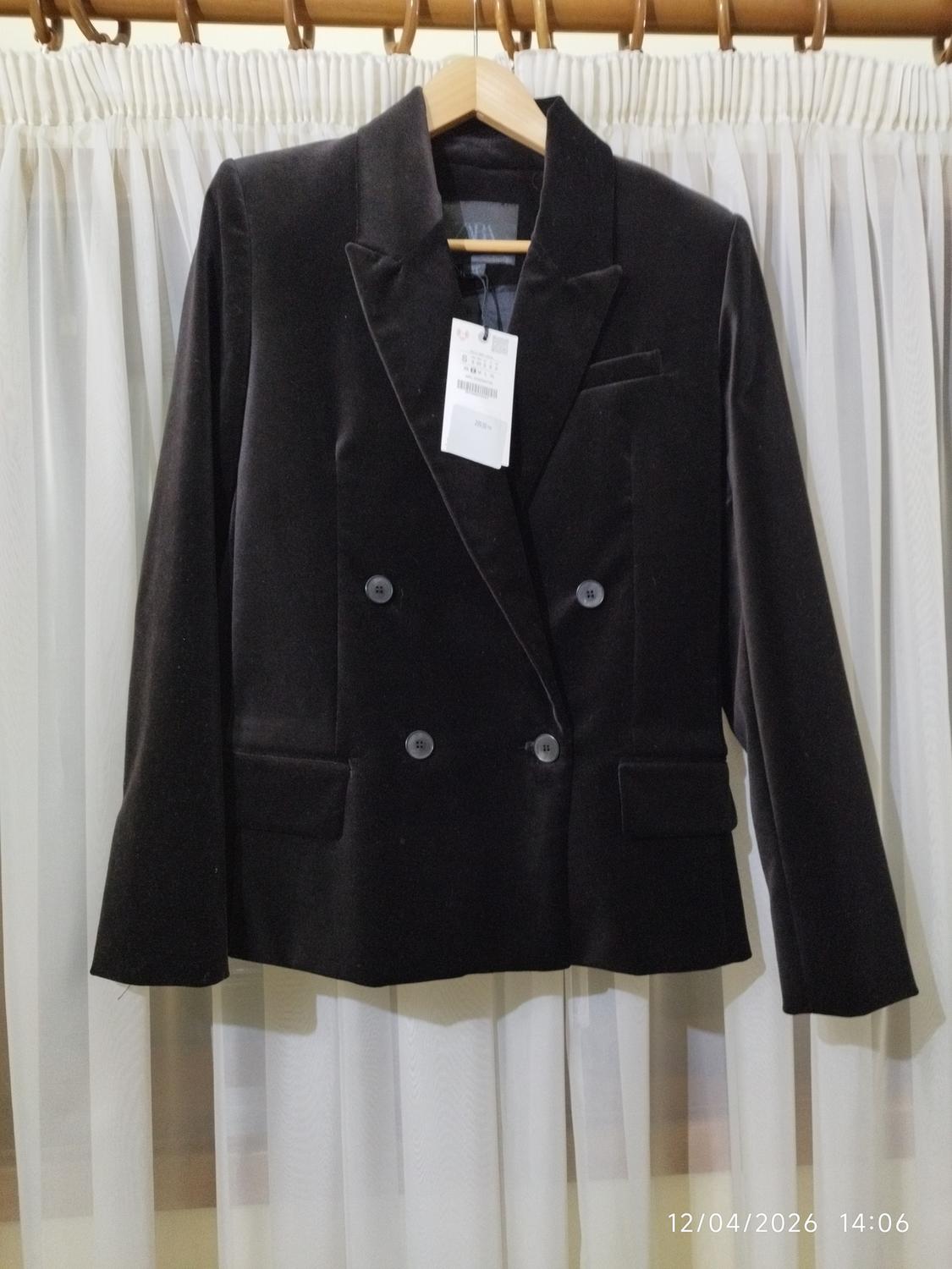 Black velvet double-breasted jacket hanging on a hanger in front of white curtains. Label visible. Date: 12/04/2026.