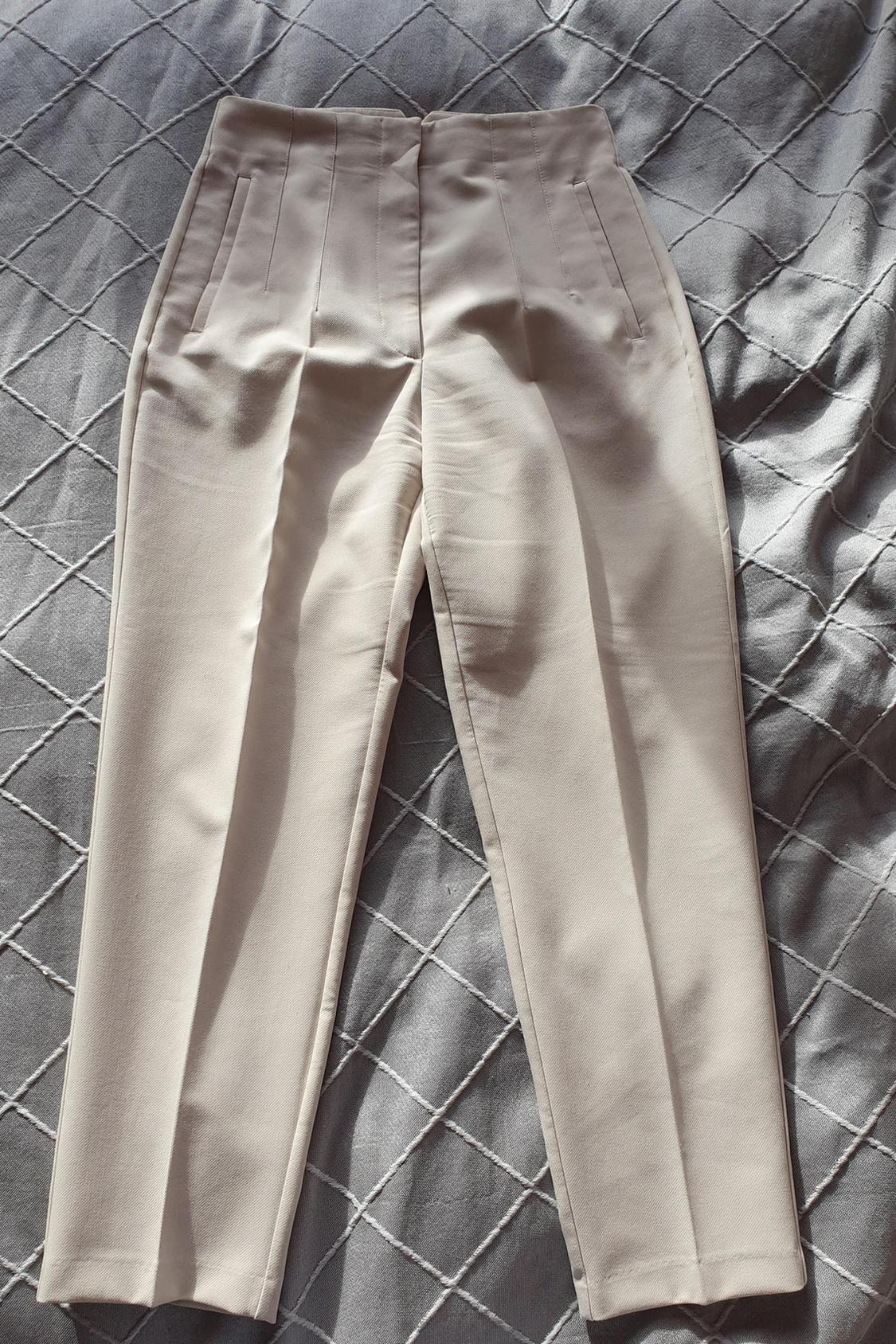 Front view of beige trousers with side pockets and a waistband with darts.