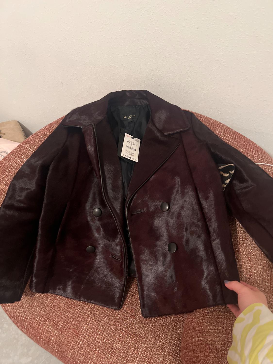 A dark brown double-breasted jacket lies on a red sofa. A hand holds the sleeve, and the label on the collar is visible.