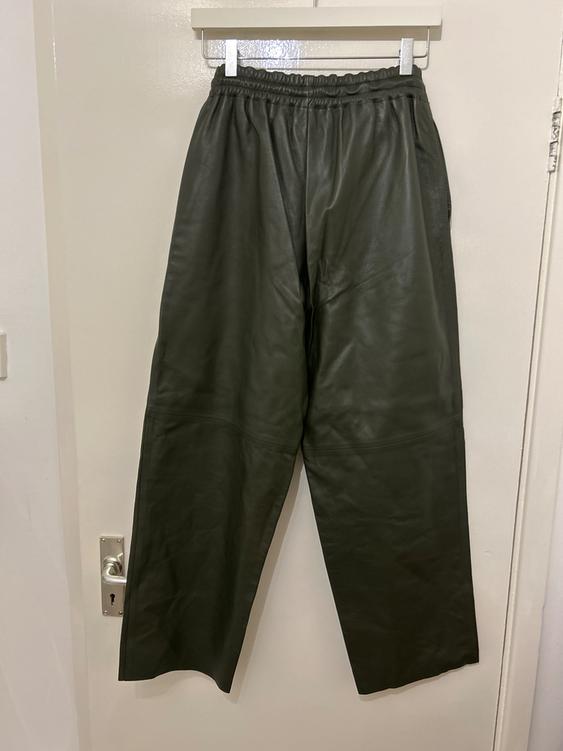 Green leather trousers hanging on a white hanger over a white door. Relaxed and modern style.