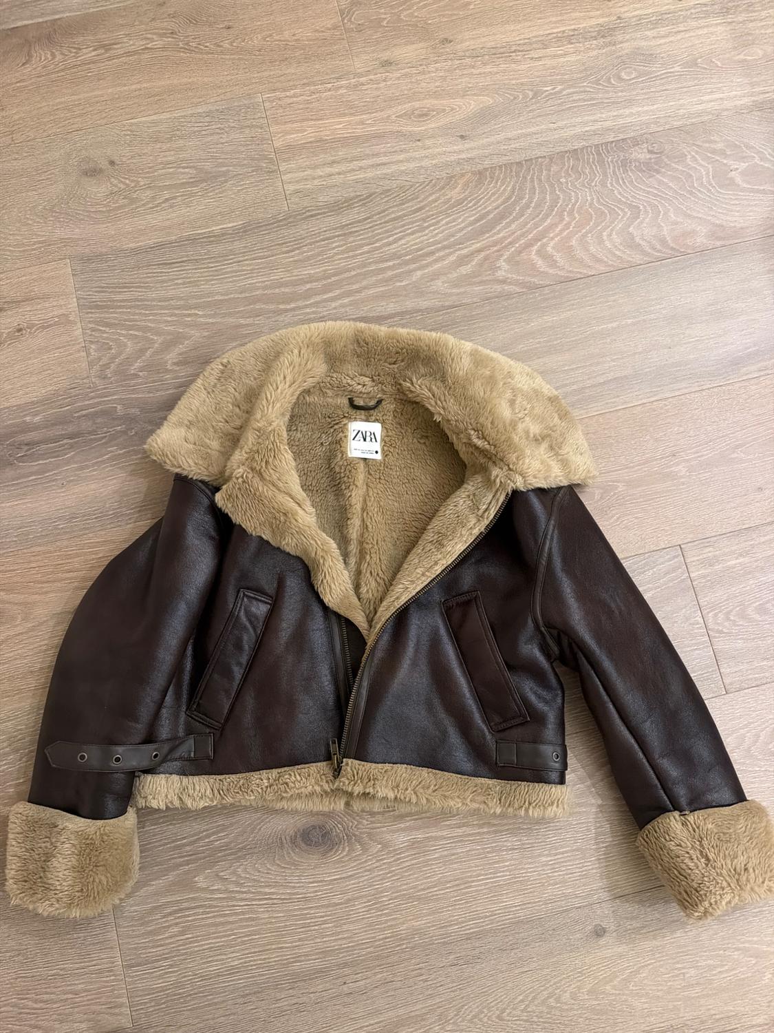 Brown jacket with a beige faux fur lining and detailing, on a wooden floor. Label with the text ZARA.
