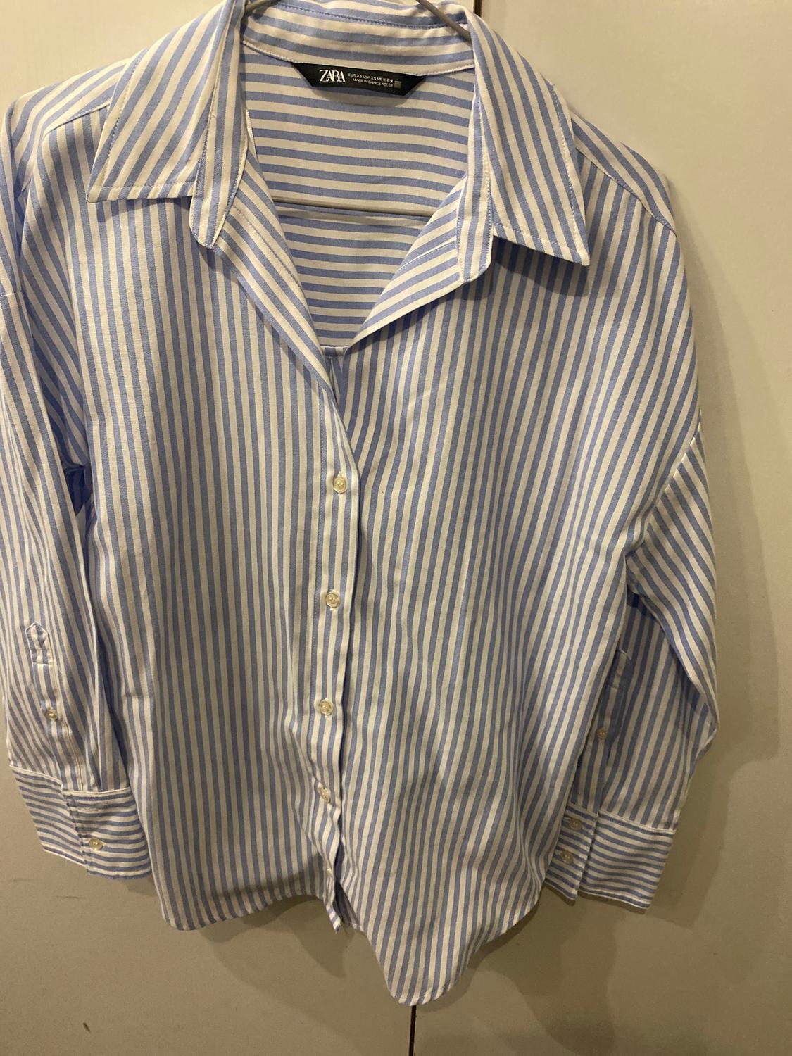 Blue and white striped shirt, hanging, with a classic collar and front buttons. Visible label: "ZARA".