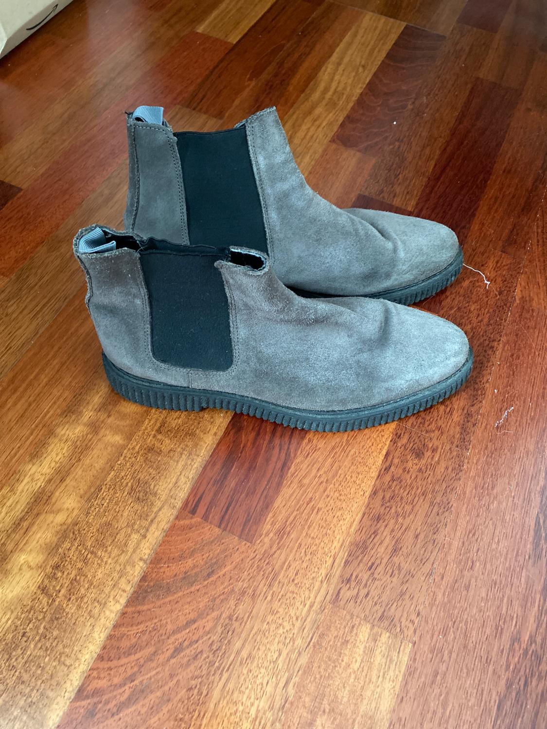 Side view of grey ankle boots with black elasticated sides and black soles on a wooden floor.