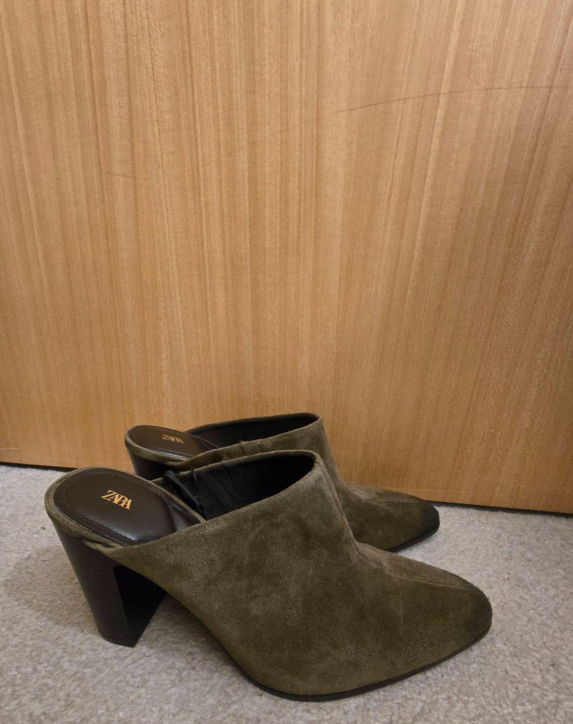 Olive green suede slingback shoes with a block heel on a rug in front of a wooden wall. ZARA text on the insole.