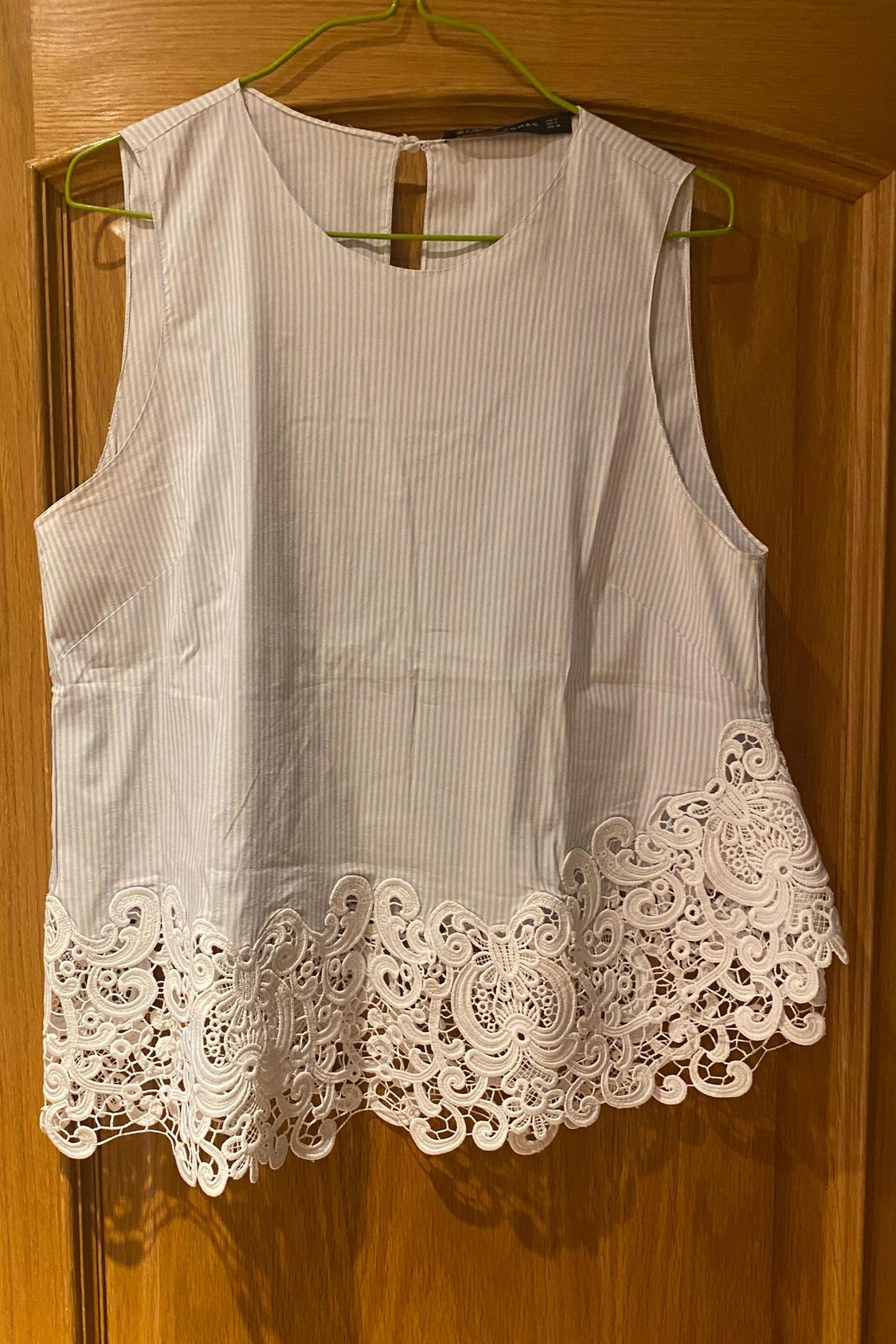 Front view of a sleeveless blouse with fine stripes and lace on the hem.
