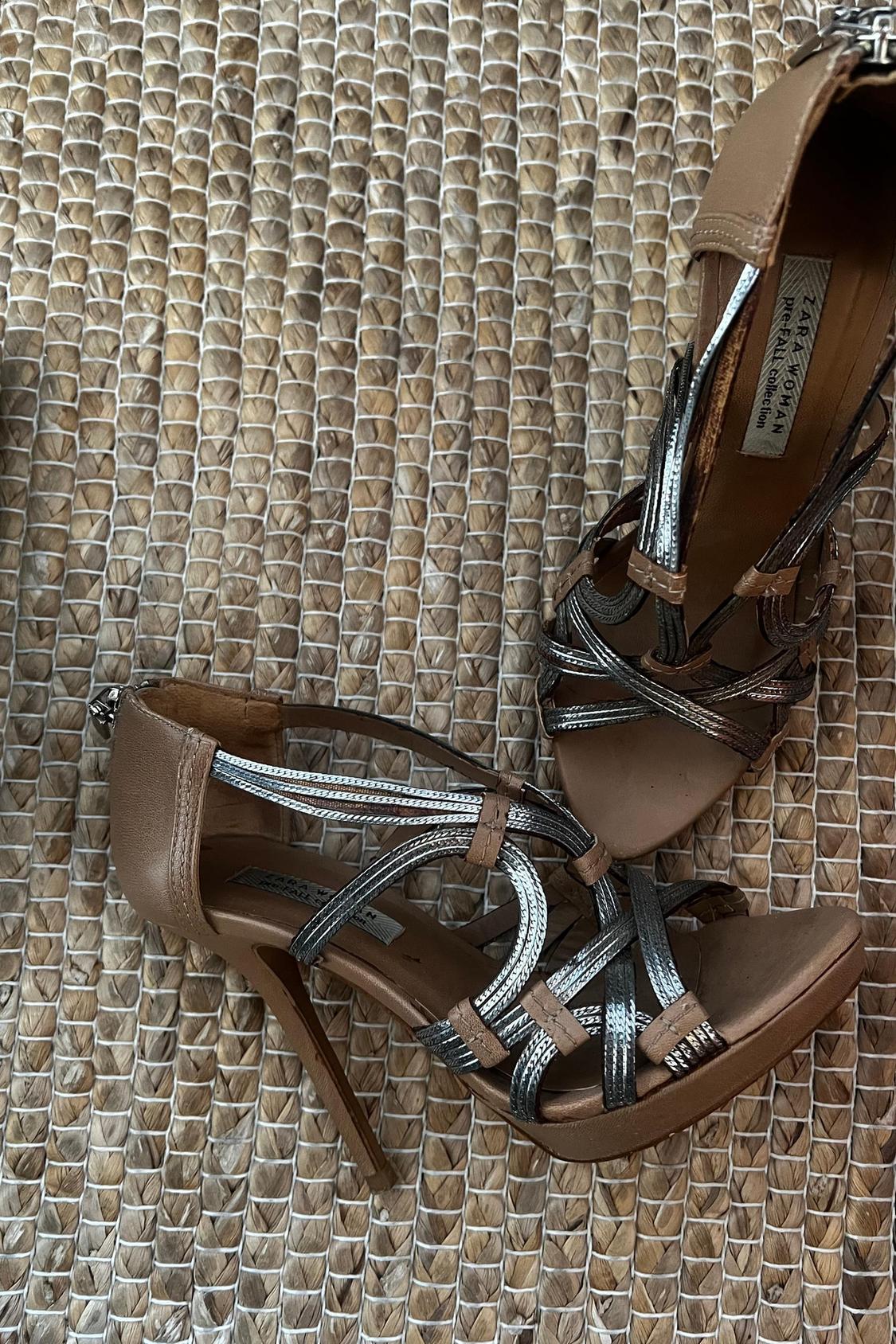 Close-up of brown heeled sandals with intertwined silver metallic straps.