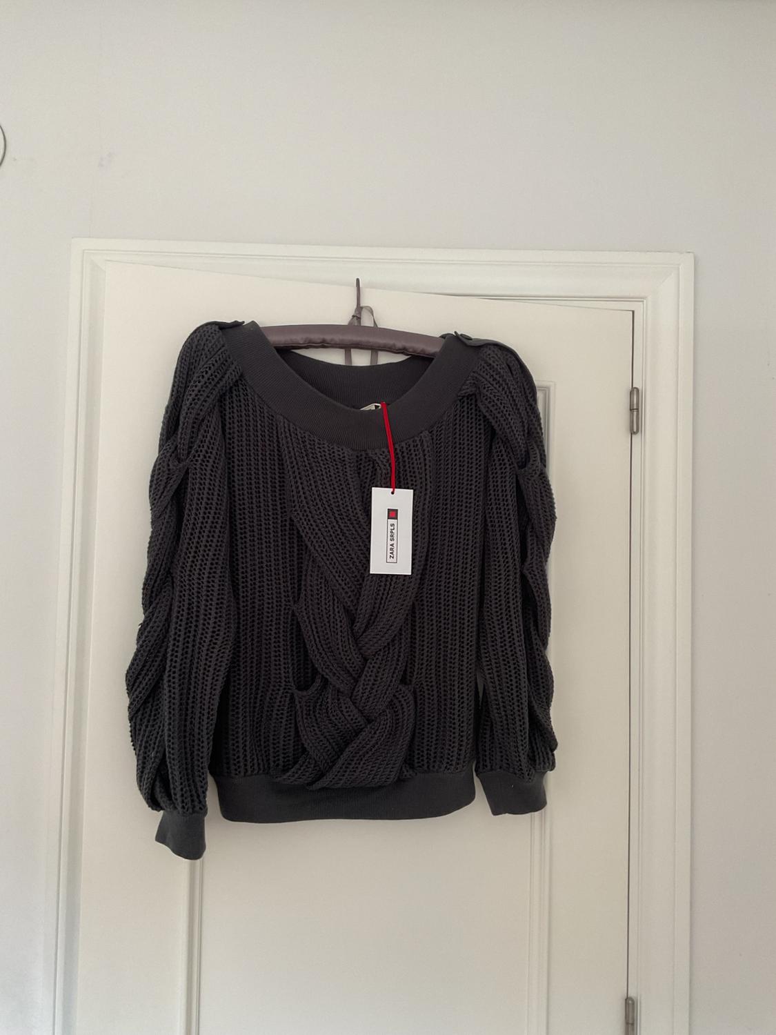 Grey chunky knit jumper hanging on a white door, with a white and red tag that says "BLACK FRIDAY".