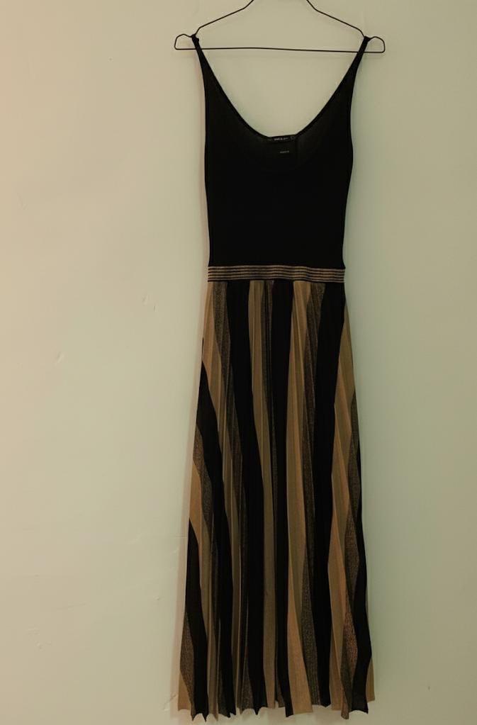 Sleeveless dress hanging on a hanger, with a black top and a pleated skirt with vertical black and beige stripes.