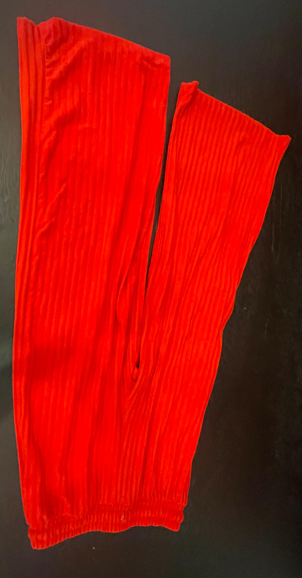Red ribbed trousers with an elasticated waistband, laid out in a relaxed style on a dark surface.