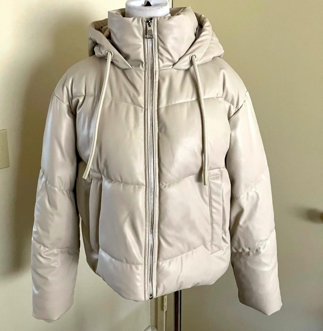 Beige padded jacket with hood and front zip fastening, displayed on a mannequin against a neutral background.