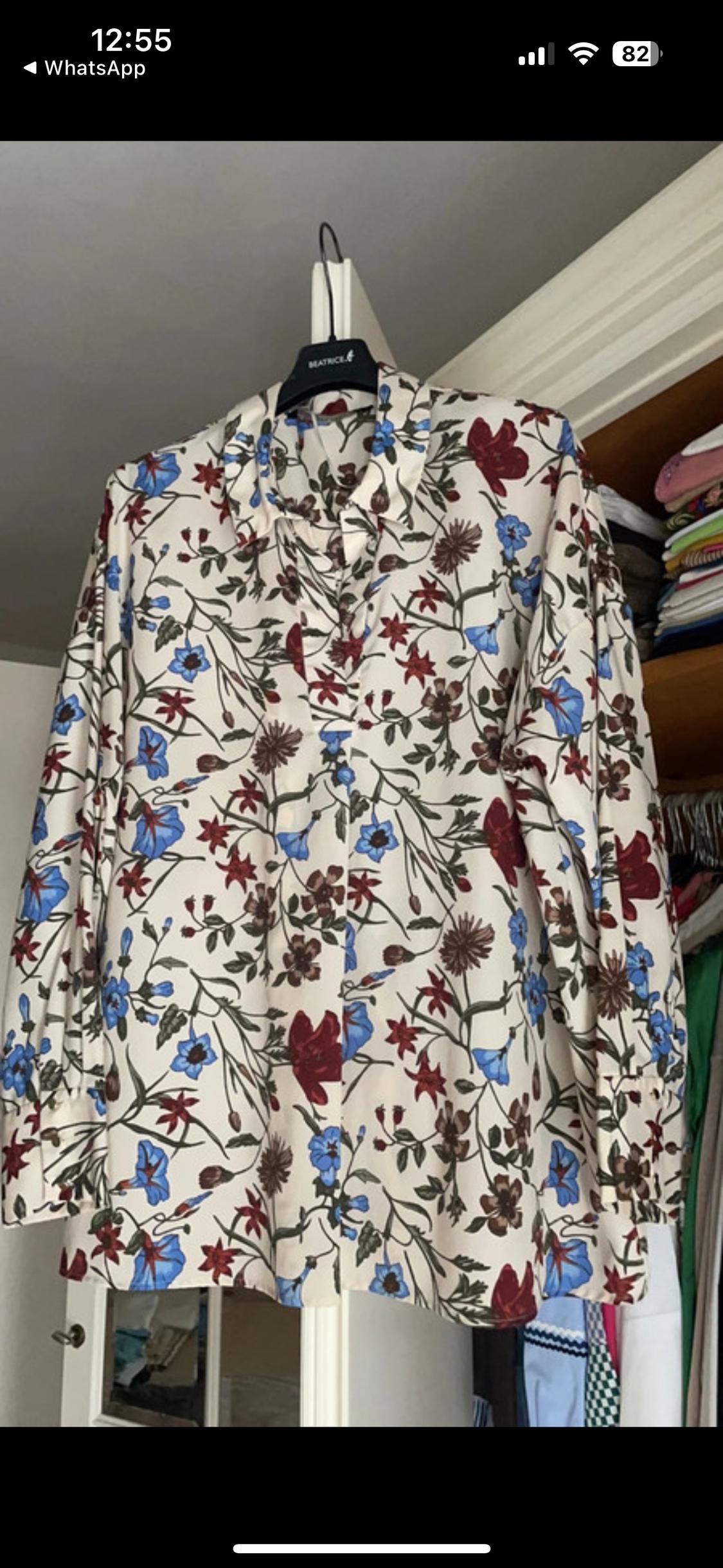 Blouse hung with a floral print in blue and red tones on a white background. Black hanger with visible "BEATRICE" text.