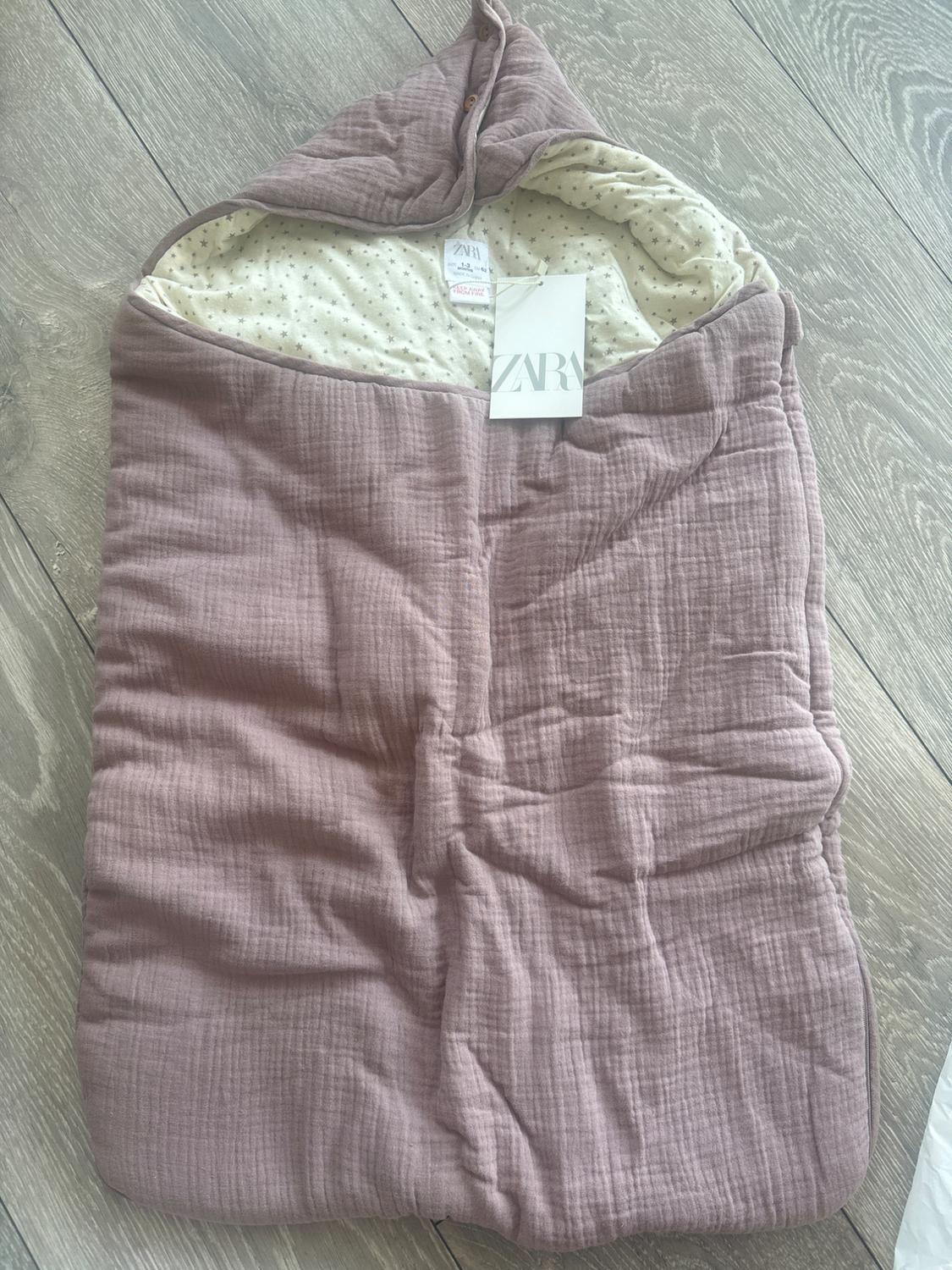 Pink crinkled-texture baby sleeping bag with a hood and star-print lining, on a wooden floor. Label with the text ZARA.