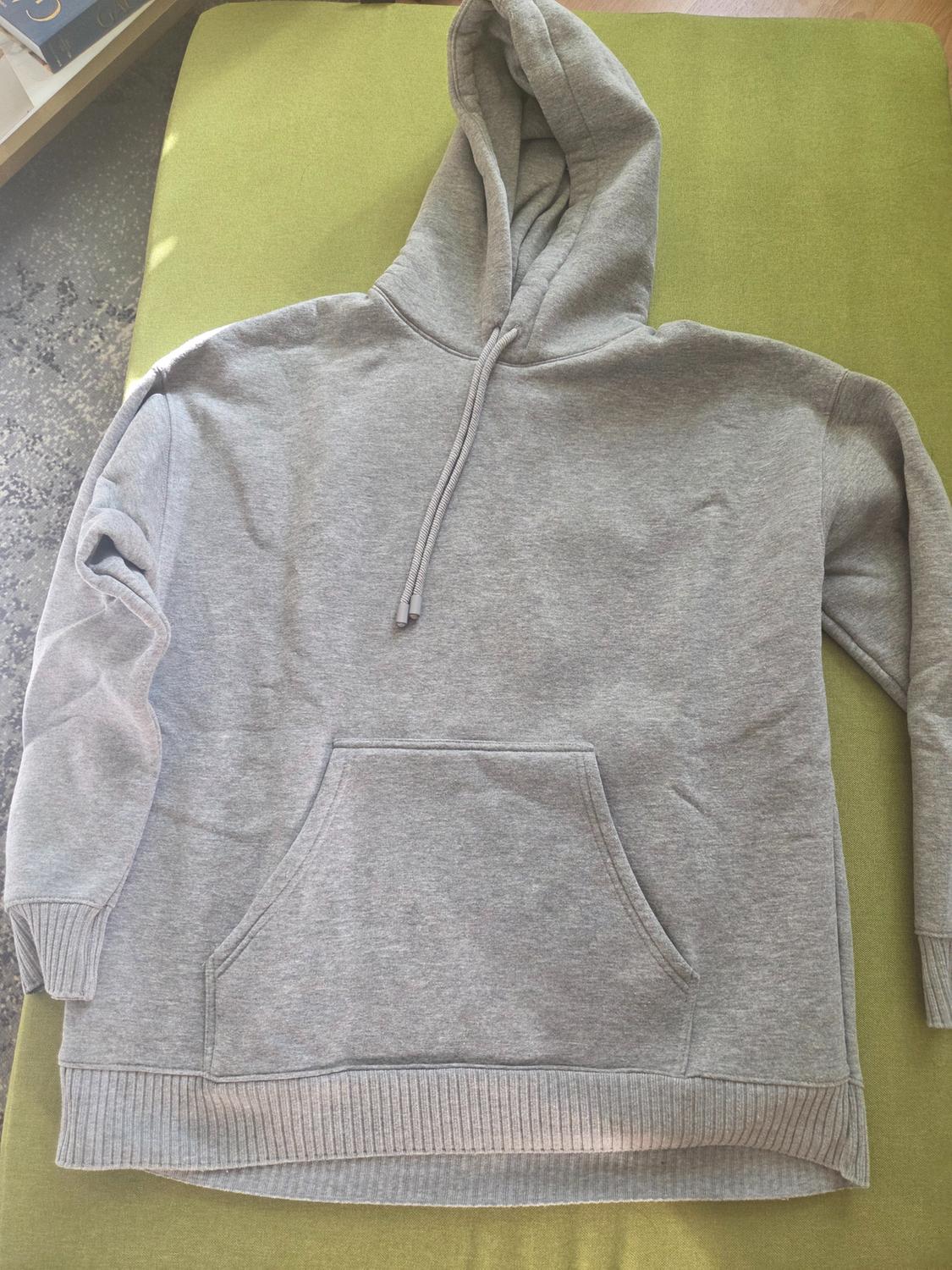 Grey hooded sweatshirt with drawstrings and a kangaroo pocket at the front, on a green surface.