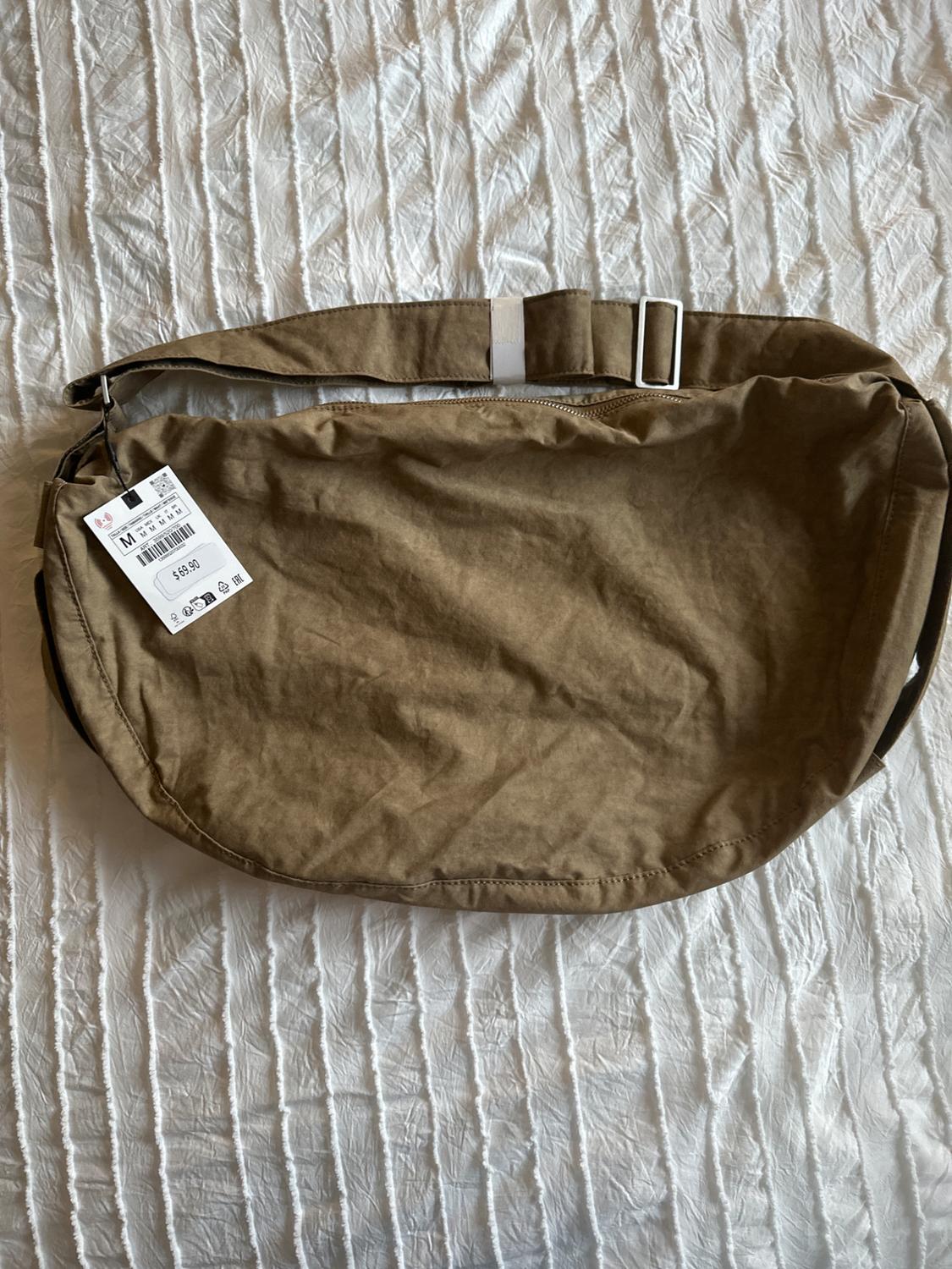 Brown handbag on a textured white bedspread. Visible tag with price of 59.99 and size M. Simple and functional design.